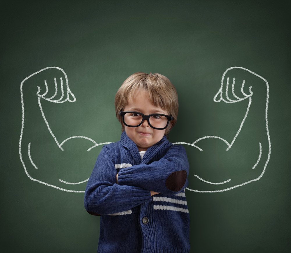 Kleiner Junge steht vor einer Tafel, auf der muskulöse Arme gezeichnet sind – Symbol für Stärke und Patient Empowerment bei Eosinophiler Ösophagitis.